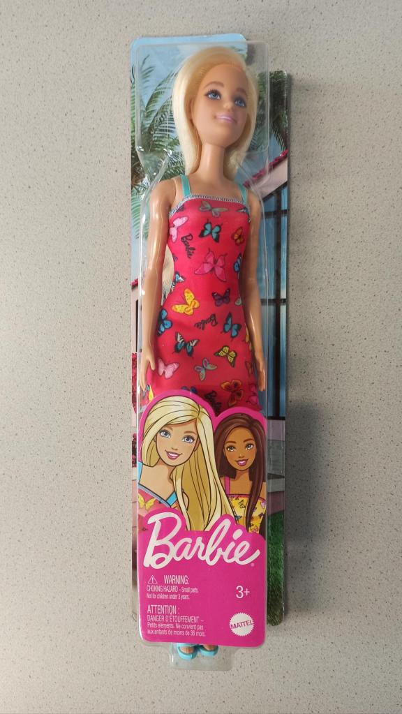 Auf dem Bild sieht man eine einzelne blonde und weiße Barbiepuppe in ihrer pinken Verpackung. Sie trägt ein pinkes Kleid mit Schmetterlingen.