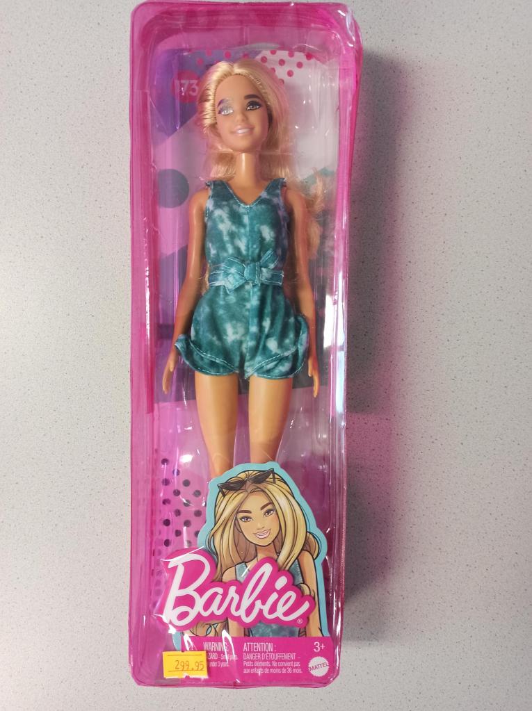 Auf diesem Foto ist eine blonde Barbiepuppe in einer pinken Reißverschlusstasche zu sehen. Sie ist braun gebrannt und trägt einen grünen Jumpsuit.